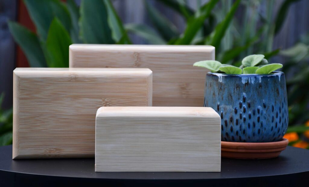Set of three bamboo slide bottom urns in different sizes, an eco-friendly upgrade option from Furevergreen Aquamation, displayed beside a blue ceramic planter with green leaves.