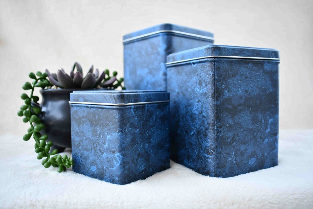 Set of three blue marble tin urns in varying sizes, part of Furevergreen Aquamation’s complimentary urn options, displayed beside a small succulent plant.