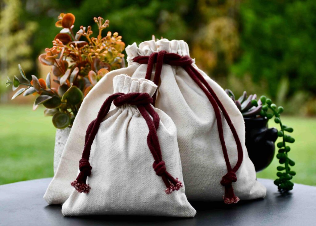 Two natural fabric drawstring bags with burgundy ties, part of Furevergreen Aquamation’s complimentary urn options, displayed beside small potted plants.